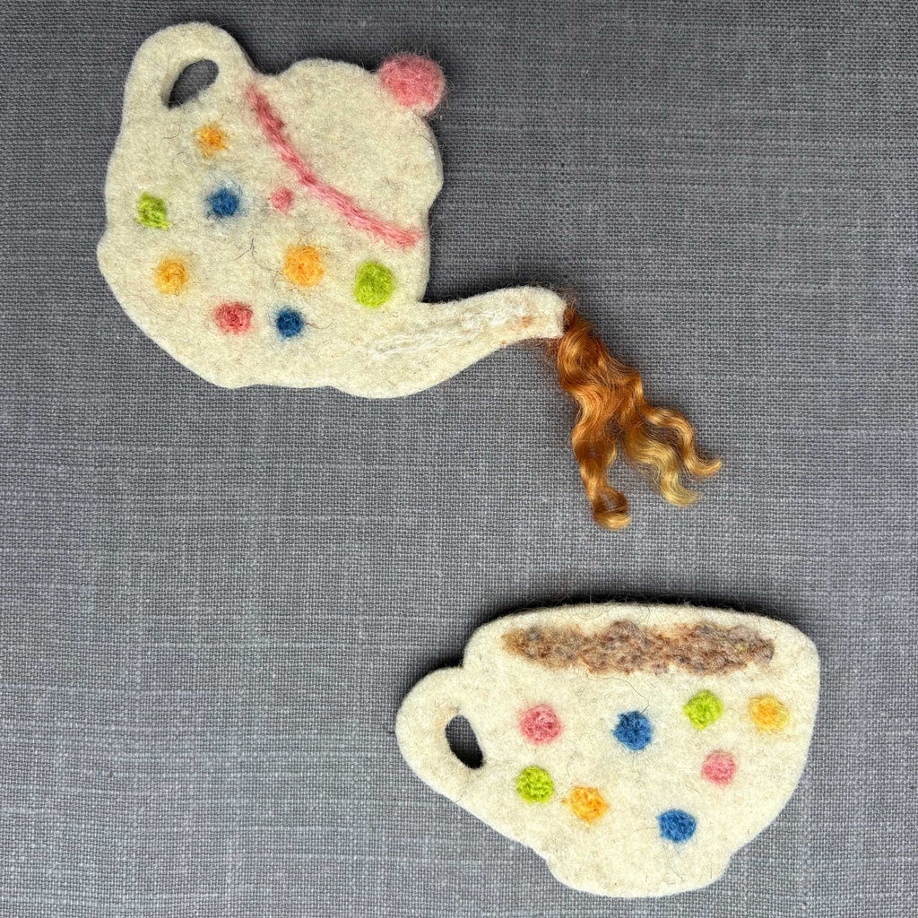 Decorative felt teapot and cup with colorful polka dots on a gray fabric background